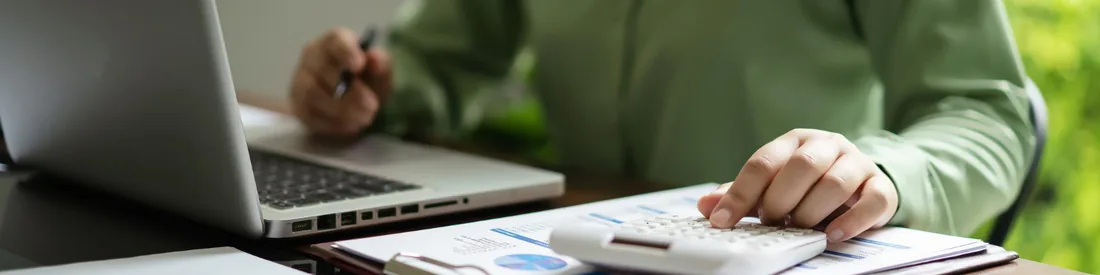 Profissional conferindo planilhas com calculadora e laptop